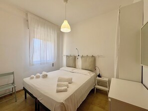 Ein Hotelzimmer mit Bett, Nachttisch, Lampe, Fenster mit Vorhängen und Spiegel.