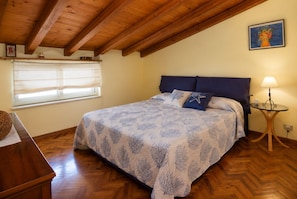 Ein Schlafzimmer mit Holzboden, einem Bett mit gemustertem Bettbezug, einem Nachttisch mit Lampe und einem Fenster mit Jalousien.
