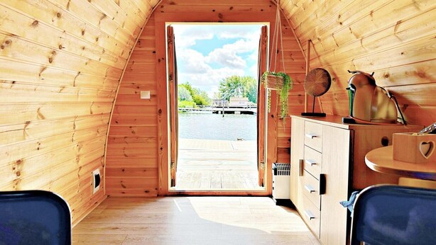 A wooden cabin interior with a view of a dock and water outside.