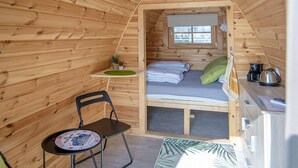 A small, wooden cabin with a loft bed, a small table with a chair, and a kitchenette area.