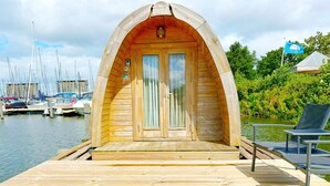 A wooden boat-shaped building with a deck, a door, and a chair.