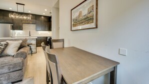 Een moderne keuken met donkere kastjes, een houten eettafel en een lijstwerk met een landschapsgezicht aan de muur.
