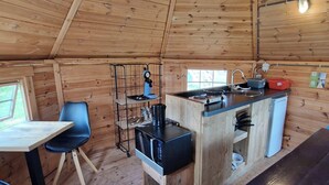 Uma cozinha compacta com paredes de madeira, uma área de refeições com mesa e cadeiras, e um frigorífico pequeno.