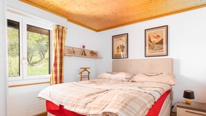 A bedroom with a bed, a nightstand, a window with curtains, and two framed pictures on the wall. - Mountain View Apartment in Grindelwald (Grindelwald)