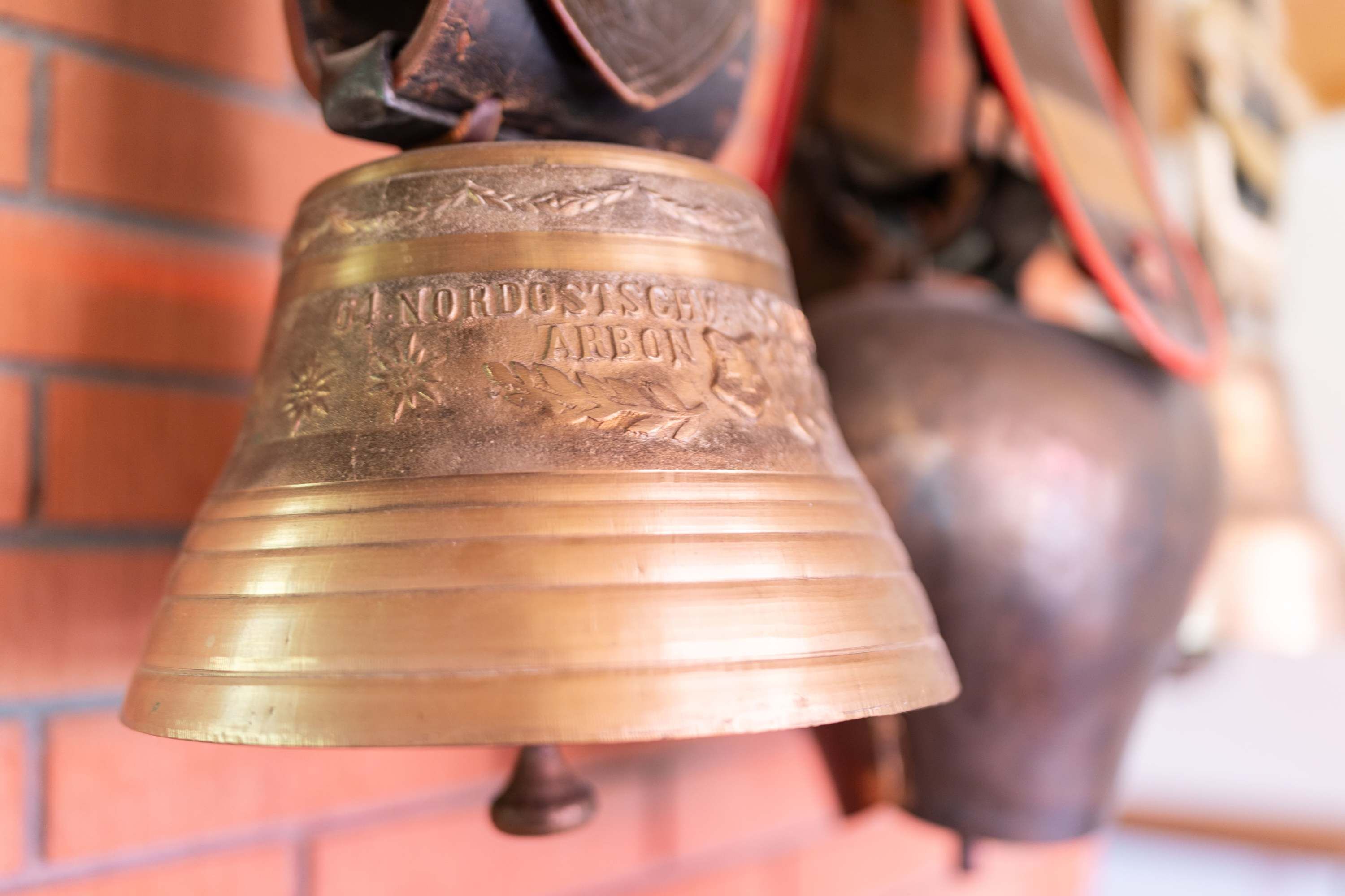 A brass bell with inscriptions, mounted on a brick wall.