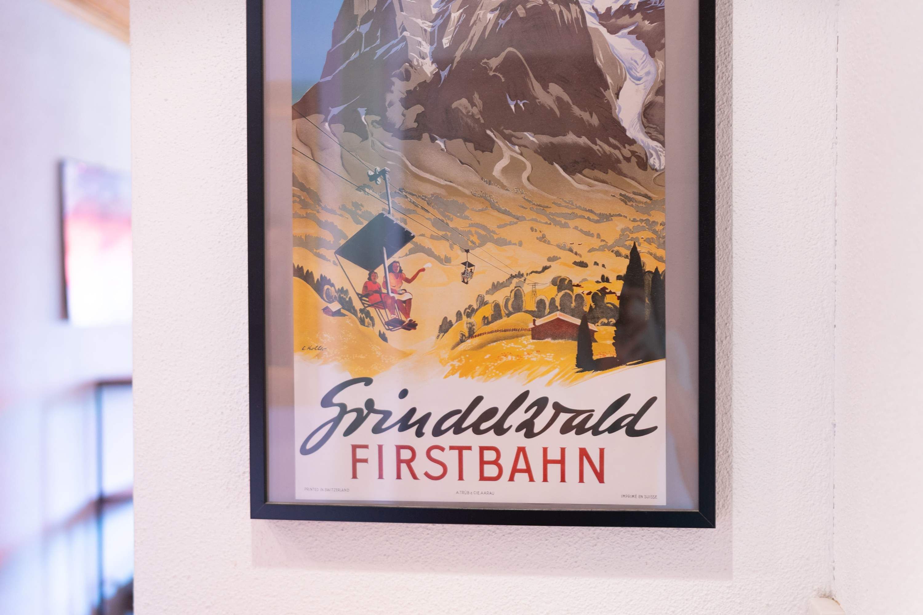 En inramad affisch med ett bergslandskap och texten ”Grindelwald FIRSTBAHN”.