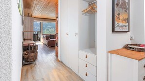 A corridor with a wooden ceiling, a white wardrobe with drawers, a wicker basket, and a framed picture on the wall. - Mountain View Apartment in Grindelwald (Grindelwald)
