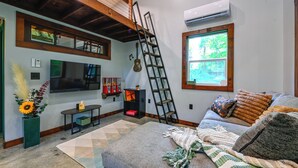 A living room with a sofa, a TV, a ladder, a window, and a fireplace. - Appalachian Cabin Haven! Gateway to Lake Linville! (Mt Vernon)