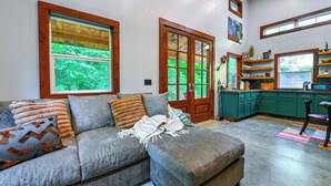 A living room with a gray sofa, a wooden door, and a kitchen with green cabinets. - Appalachian Cabin Haven! Gateway to Lake Linville! (Mt Vernon)