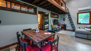 A dining area with a wooden table and red chairs, a staircase, and a view of the outdoors. - Appalachian Cabin Haven! Gateway to Lake Linville! (Mt Vernon)