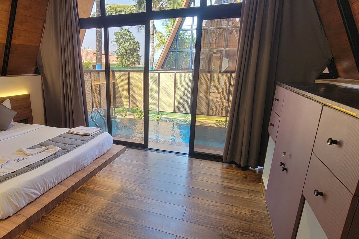 Un dormitorio con cama, piso de madera, cortinas y vistas a una piscina.