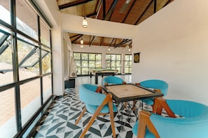 A room with large windows, a pool table, and blue chairs. - Evo Farmstay (Karjat)