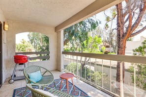 Ein Balkon mit Grill, Stühlen und Blick auf Bäume und Gebäude.