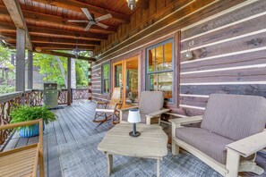A wooden deck with outdoor furniture, including a rocking chair and a sofa, and a table with a lamp. - Franklin Cabin w/ Hot Tub, Theater & Fire Pit! (Franklin)