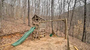 Una struttura giochi in legno con uno scivolo in una zona boschiva.