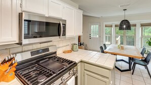 A kitchen with white cabinets, a stainless steel microwave, a gas stove, and a dining table with chairs. - Pet-Friendly Yard w/ Hot Tub! Peaceful Austin Home (Austin)