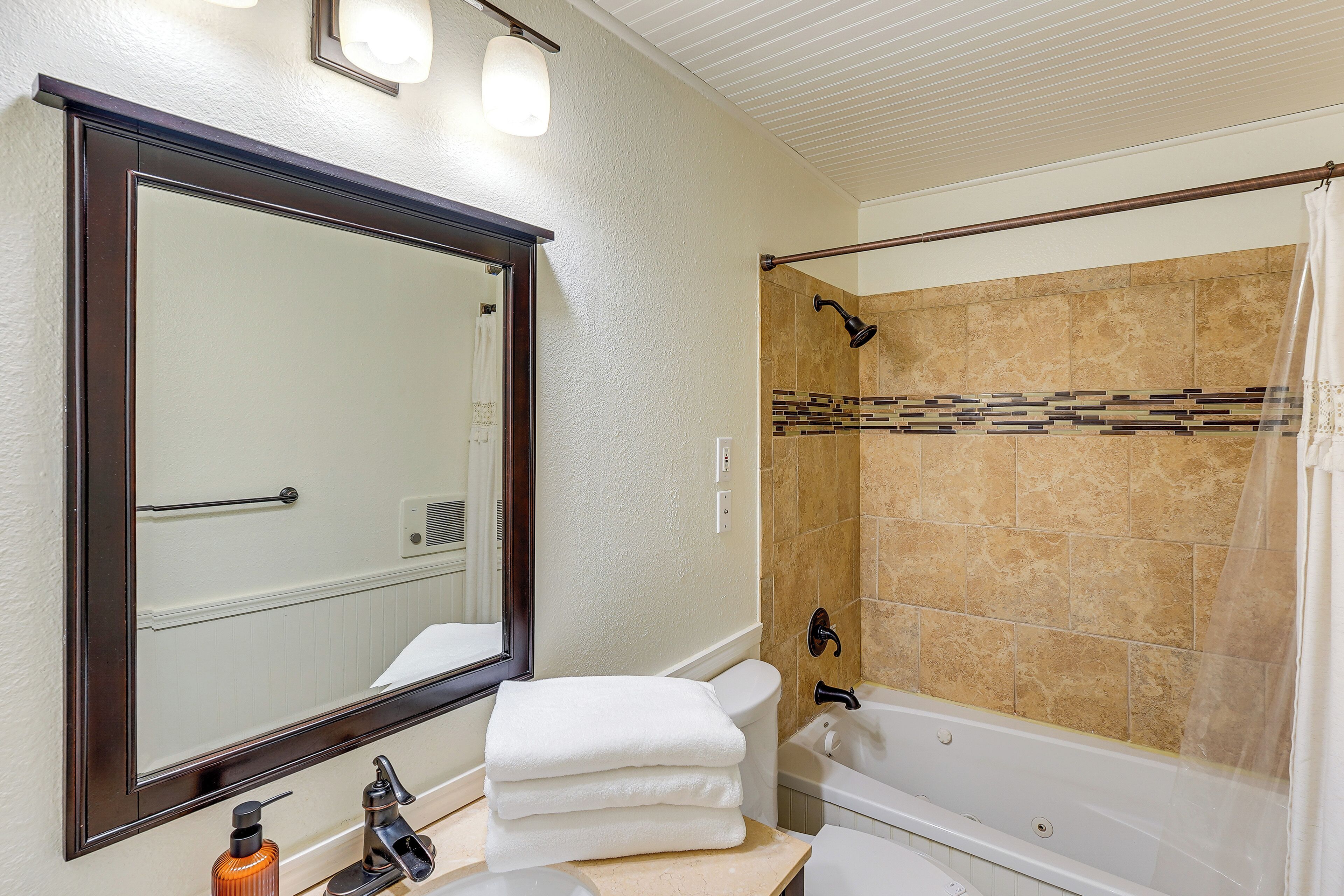 Ein Badezimmer mit großem Spiegel, einer Badewanne, einer Dusche und einem Stapel Handtücher.