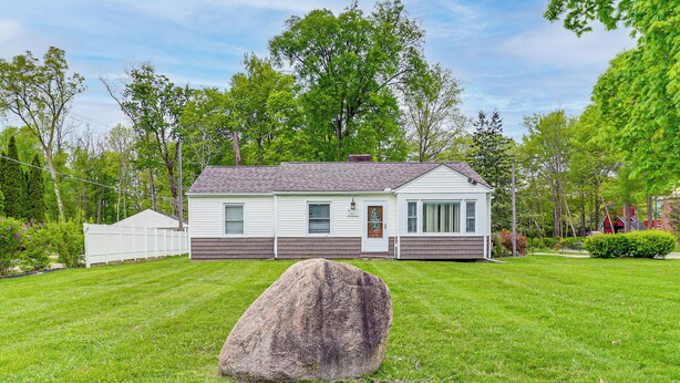 Une maison de plain-pied avec un jardin devant, un grand rocher au premier plan et une clôture blanche en bois.