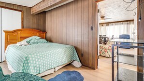 Une chambre à coucher avec une tête de lit en bois, une couvre-lit à motifs verts, un tapis bleu et une table en verre.