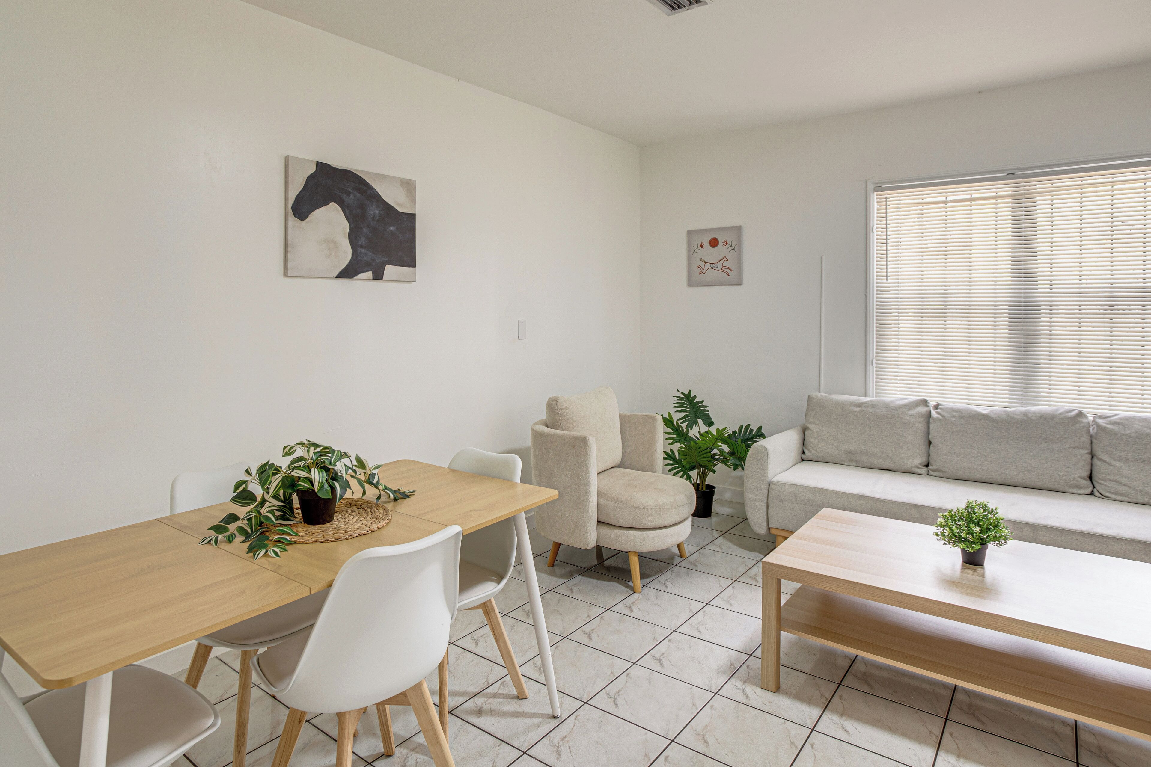A modern living room with a dining area, a sofa, and two potted plants.