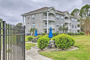 A multi-story building with a stone facade, balconies, and outdoor seating areas with blue umbrellas. - Pool Access! Myrtlewood Villas Golf Escape (Myrtle Beach)