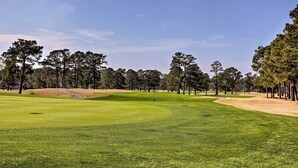 Un campo de golf con un green impecable, búnkeres de arena y cielo despejado.