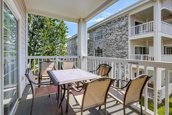 A covered outdoor area with a table and chairs, a balcony railing, and a stone building in the background. - Pool Access! Myrtlewood Villas Golf Escape (Myrtle Beach)