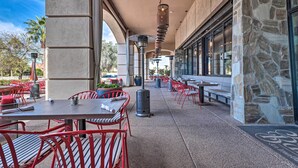 Ein Außenbereich mit einer Terrasse, rotem Metallmobiliar, Steinsäulen und freiem Blick auf die Straße.