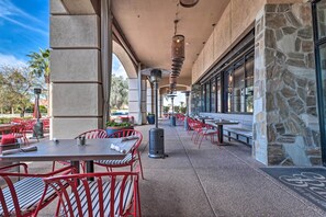 Eine Außenpatio-Terrasse mit roten Metallstühlen und -tischen, Steinmauern und blauem Himmel.