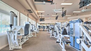 Ein Fitnessraum mit verschiedenen Trainingsgeräten, großen Fenstern und Deckenventilatoren.