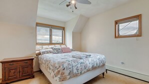 Ein Schlafzimmer mit einem Bett, einer Holzkommode, einem Deckenventilator und einem Fenster.