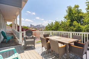 Eine überdachte Terrasse im Freien mit Korbmöbeln und Blick auf eine Stadtsilhouette.