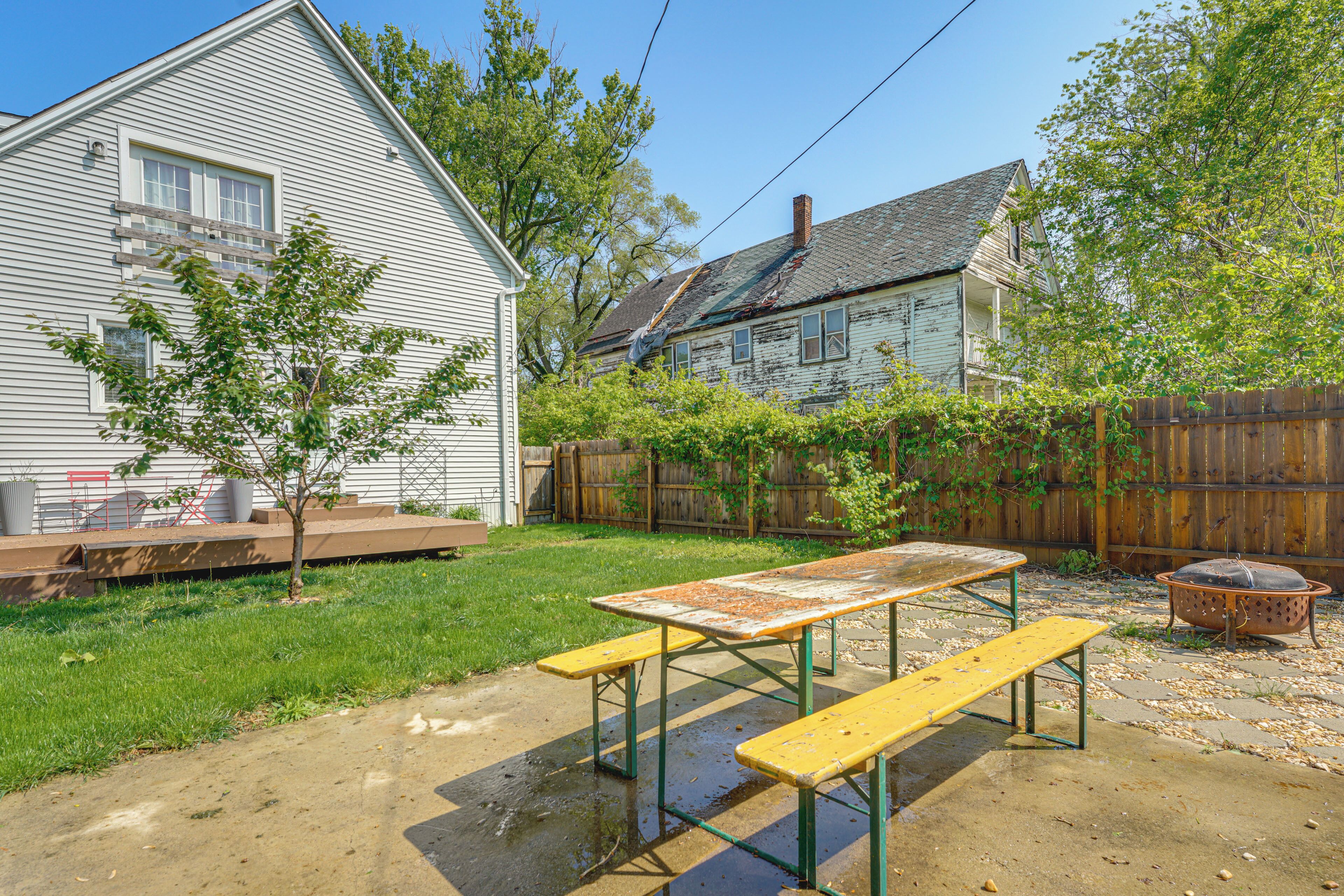 Un jardin avec une table de pique-nique, un banc en bois, un petit arbre et une clôture en bois.
