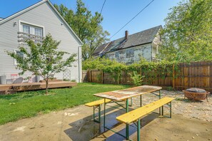 Un jardin avec une table de pique-nique, un banc en bois, un petit arbre et une clôture en bois.