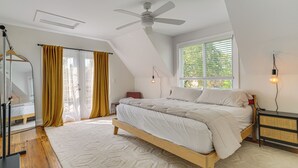 Un dormitorio con una cama, ventilador de techo, ventana con persianas, mesita de noche y lámpara.