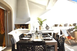 An outdoor dining area with a table set for four, surrounded by chairs, a potted plant, and a brick wall. - Seafront Palatino Apartment for 8 (Martigues)