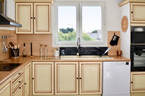 Een keuken met houten kastjes, een vaatwasser en een raam met uitzicht op groen.