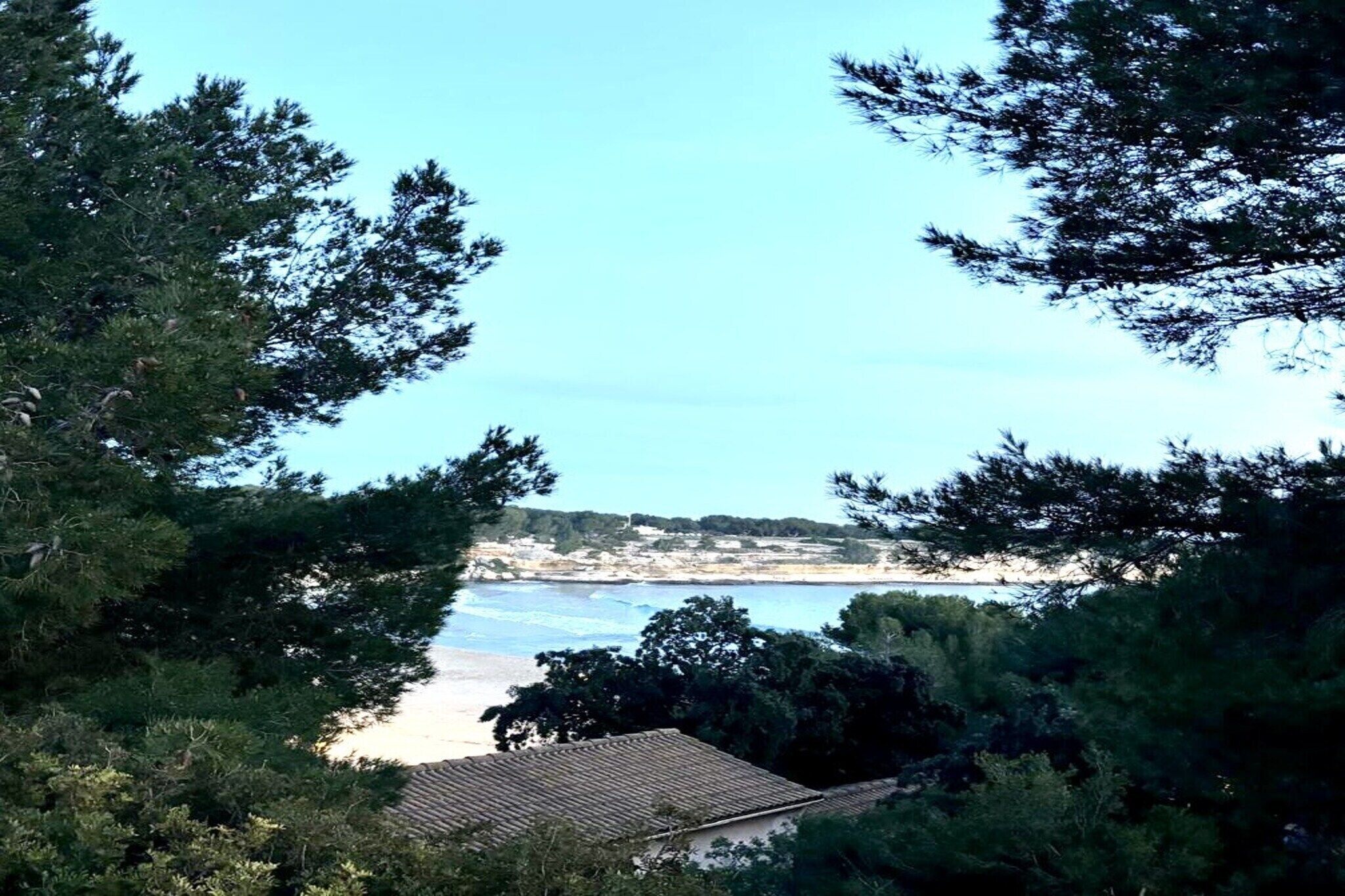 A coastal view with a beach, trees, and a building with a tiled roof.