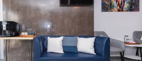 A modern living room with a blue sofa, a coffee machine, a TV, and a painting on the wall.