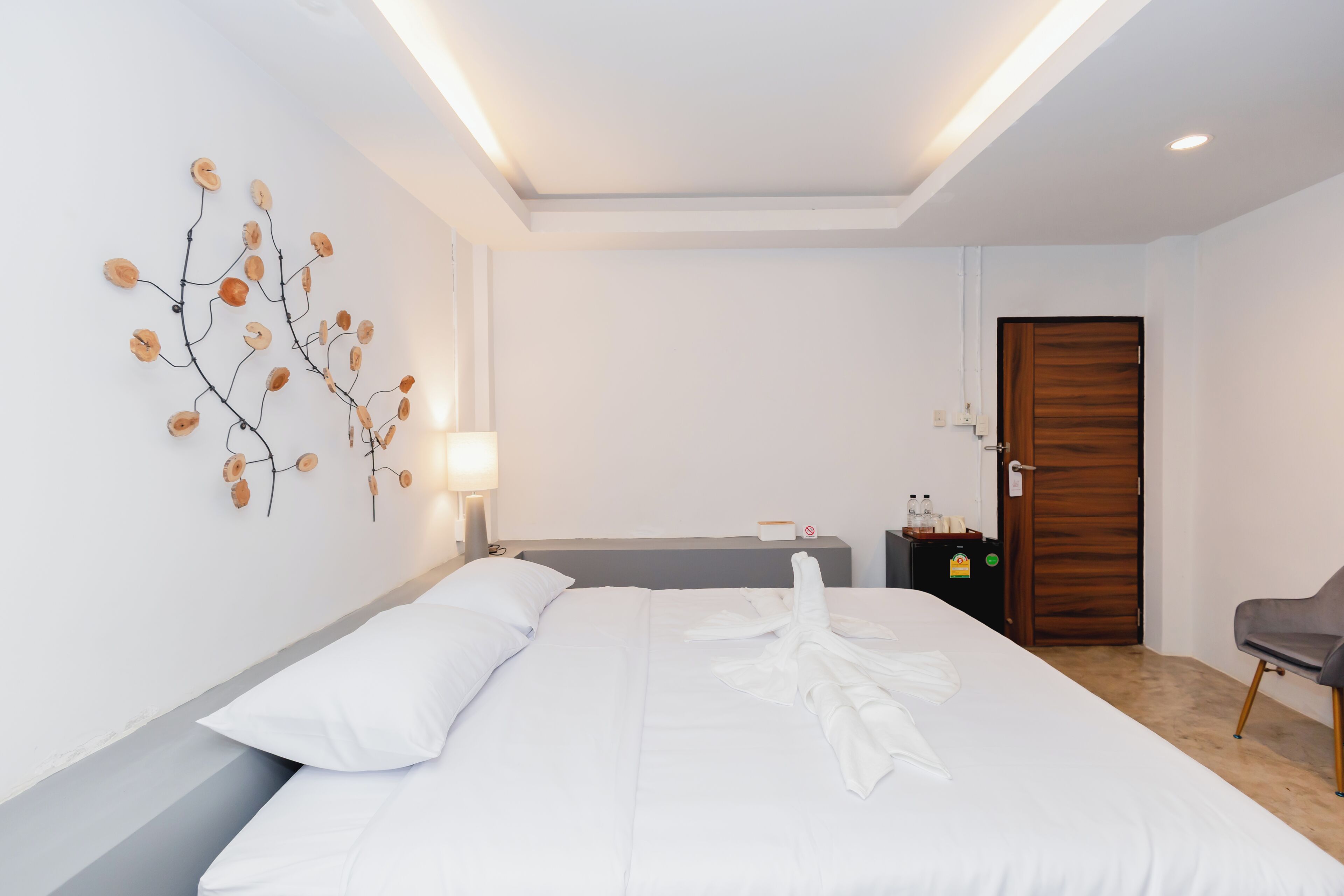 A hotel room with a neatly made bed, a wall-mounted art piece, a bedside table with a lamp, and a door with a wooden frame.