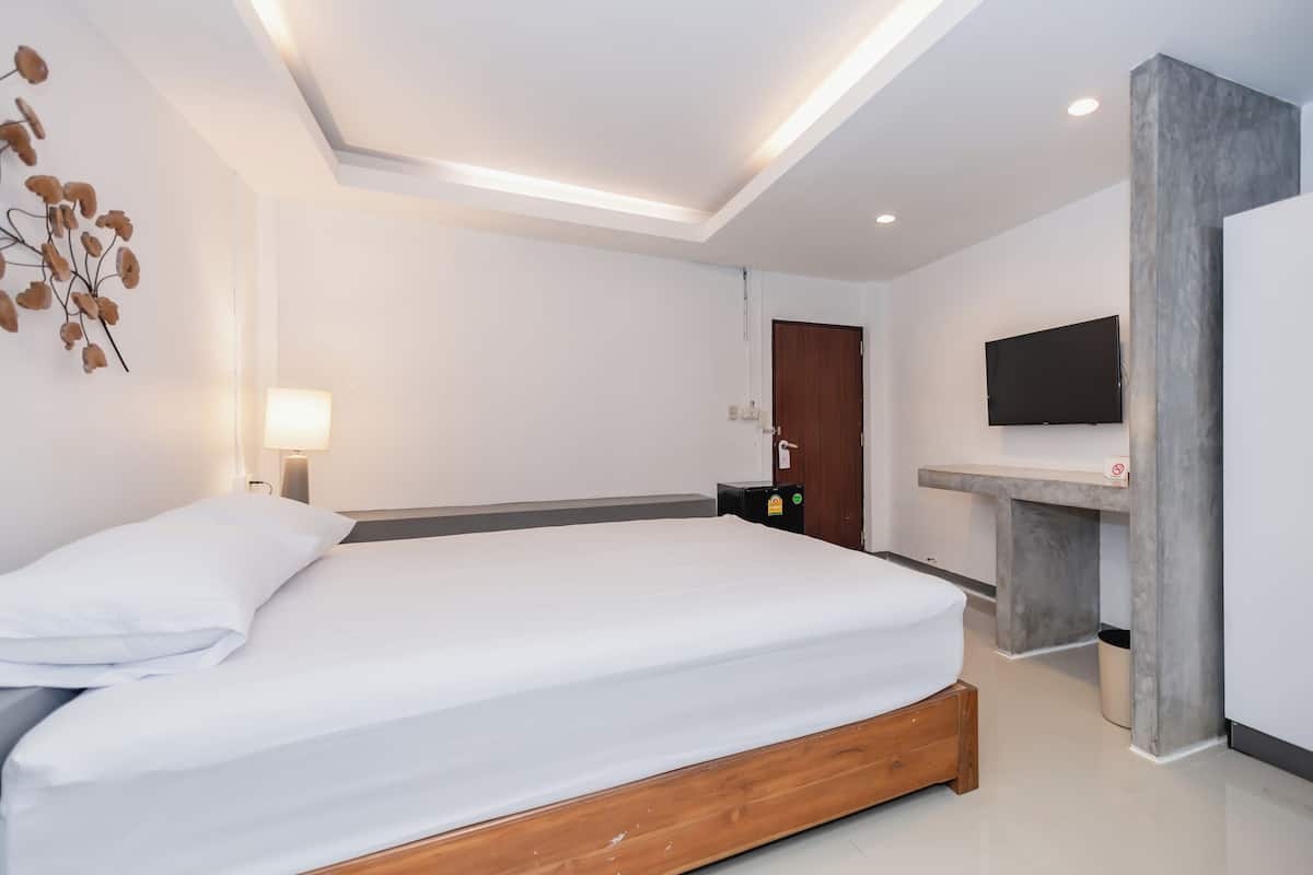 A modern hotel room with a large bed, a flat-screen TV mounted on the wall, a bedside table, and a built-in bench.