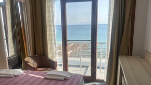 A hotel room with a bed, a chair, a desk, and a large window with a view of the sea. - Sultans And Kings Hotel (Didim)