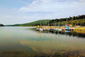Ein ruhiger See mit Booten, die an einer Anlegestelle liegen, umgeben von Grünflächen und Hügeln.
