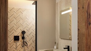 Um banheiro moderno com parede de chuveiro em padrão herringbone, porta de madeira, pia de mármore e espelho com moldura de madeira.