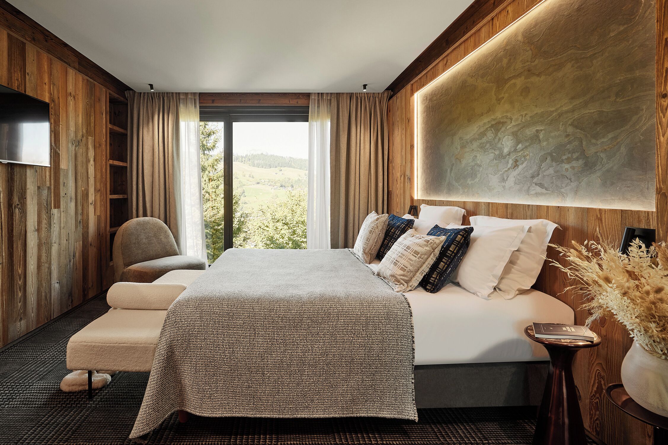 Une chambre à coucher avec un grand lit, une chaise, une table de chevet et une vue sur l’extérieur.