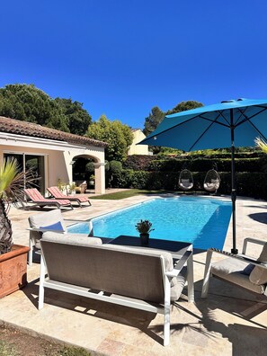 Ein Swimmingpool mit Liegestühlen und einem Sonnenschirm, umgeben von einem Garten und einem Gebäude.