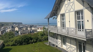 En toetages bygning med balkon, fri udsigt over havet og en by i baggrunden.