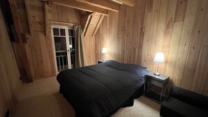 Et soveværelse med en stor seng, to sengeborde med lamper, et træloft og en skydedør af glas til et udendørs område.