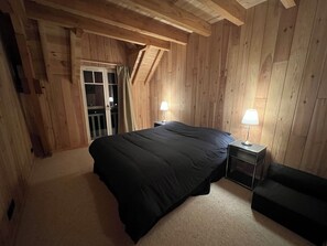 A bedroom with a large bed, two bedside tables with lamps, a wooden ceiling, and a sliding glass door leading to an outdoor area. - Normandy seaside villa with view and terrace 5 minutes walk from the beach (Arromanches-les-Bains)