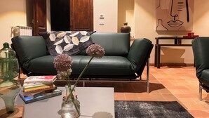 Un salon avec un canapé en cuir vert, une table basse sur laquelle sont posés des livres et un vase, un tableau au mur et un sol carrelé.